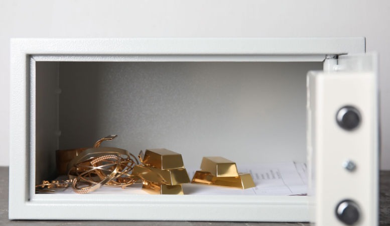 open safety box with gold bars and jewelries on gray table