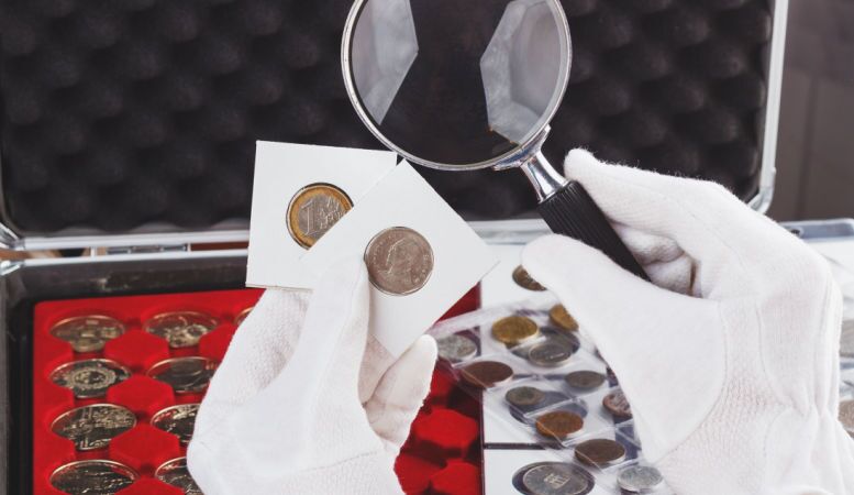 hands with gloves hold magnifying glass and gold collector coins