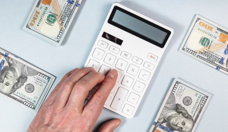 man using calculator surrounding with hundred dollar bills