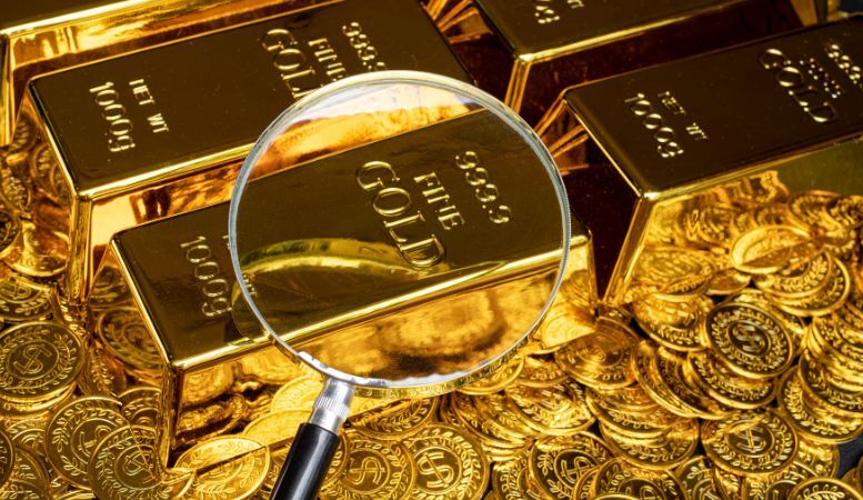 magnifying glass on pile of gold bars and gold coins